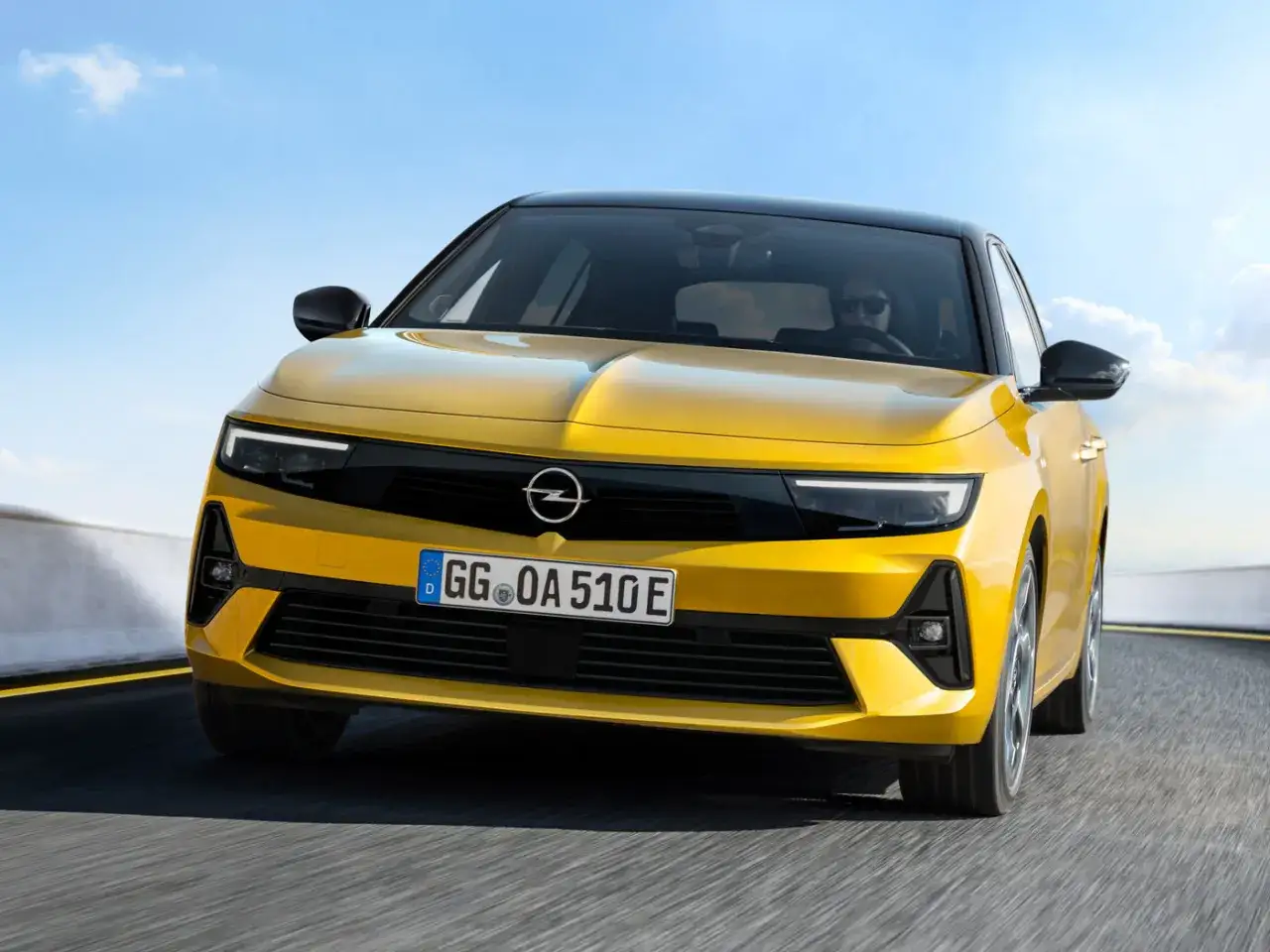 Żółta Opel Astra 2025 z czarnym dachem pędzi po drodze, prezentując nowoczesny design i dynamiczną sylwetkę.