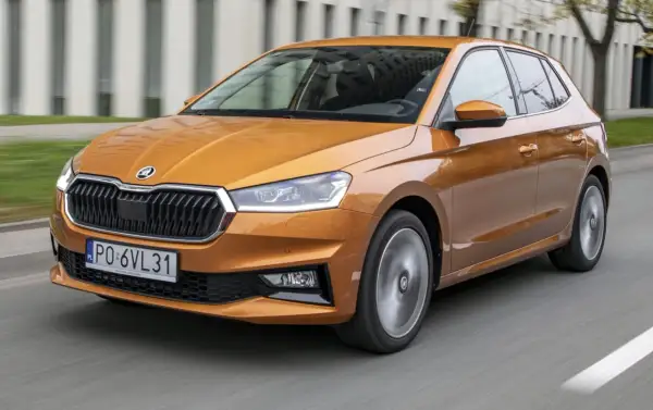 Pomarańczowa Skoda Fabia 2021 pędzi po drodze, jej reflektory ostro świecą, a felgi wirują w ruchu.