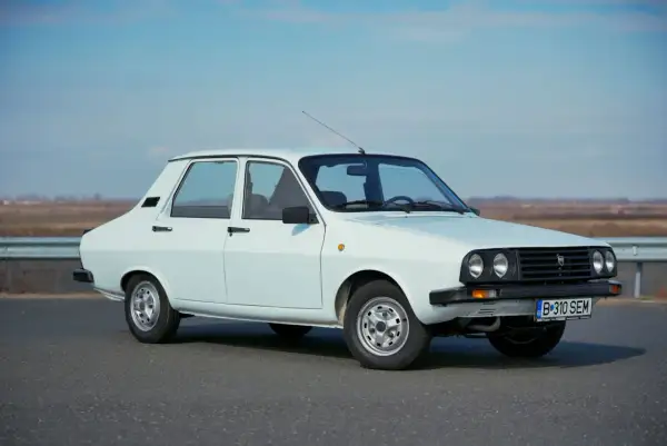 Biała Dacia 1300 stoi na drodze, gotowa na podróż. Klasyczny design i proste linie tego samochodu przyciągają wzrok.