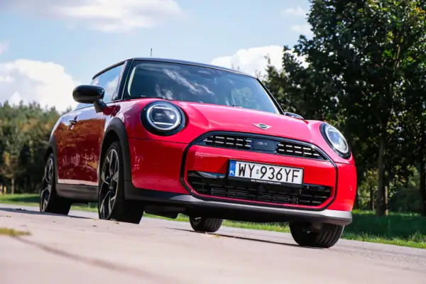 Czerwony Mini Cooper na tle zieleni. Wiele osób szuka opinii o tym modelu, a ten egzemplarz wygląda na gotowy do jazdy.