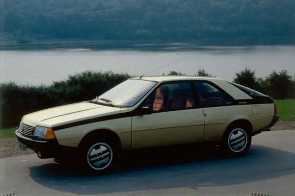 Złoty Renault Fuego z czarnymi pasami na boku, zaparkowany nad jeziorem.