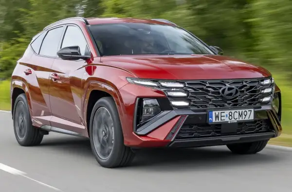 Czerwony Hyundai Tucson N Line, nowoczesna hybryda, pędzi po drodze, otoczony zielenią.