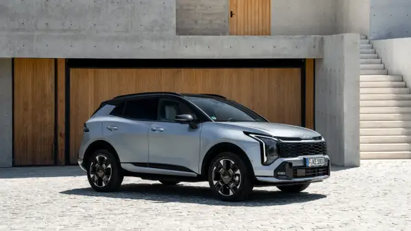 Srebrna Kia Sportage hybryda zaparkowana przed nowoczesnym budynkiem z drewnianymi drzwiami i betonowymi schodami.
