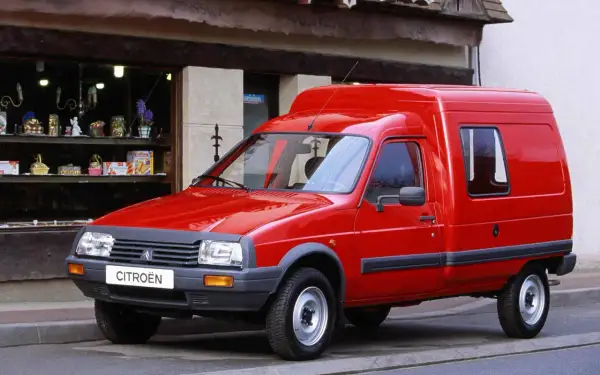 Czerwony Citroen C15, dostawczy klasyk, parkuje przed sklepem z upominkami.