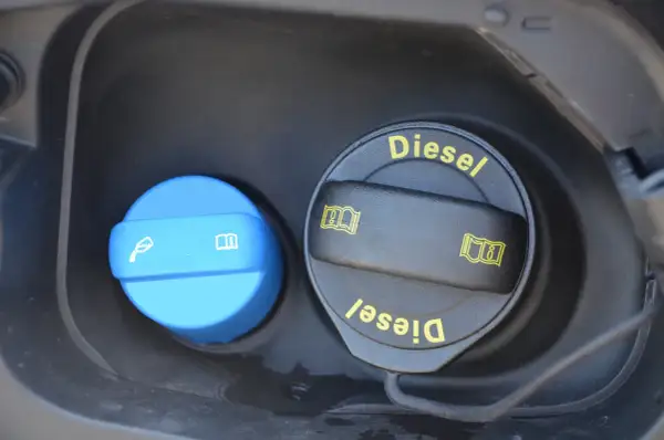 Dwa korki wlewu paliwa: jeden niebieski z symbolem płynu i książki, drugi czarny z napisem "Diesel" i symbolami. Dowiedz się, adblue co to jest i do czego służy.