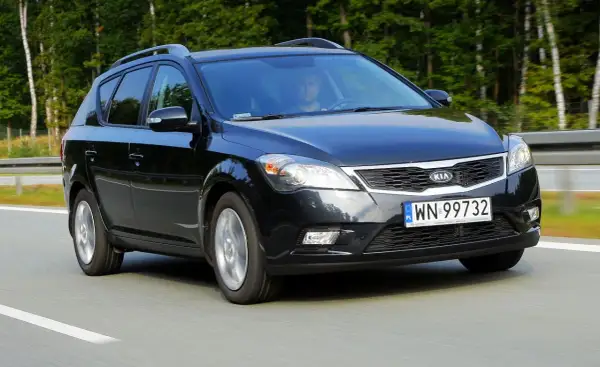 Czarny Kia Ceed 1. kombi jedzie po drodze, otoczony zielenią.
