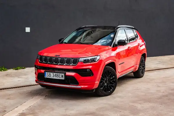 Czerwony Jeep Compass z czarnym dachem i felgami. Zbliżenie na przód auta, gdzie widoczne są charakterystyczne siedmioszczelinowe wloty powietrza. Idealny do miasta i na wyprawy, jego wymiary są dopasowane do potrzeb kierowców.