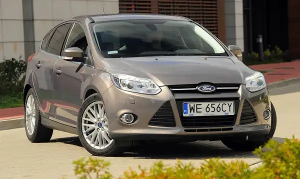 Brązowy Ford Focus 2014, zaparkowany przed nowoczesnym budynkiem, gotowy do podróży.