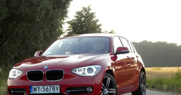 Czerwone BMW 118d na tle drzew i pól.