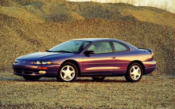 Fioletowy Dodge Avenger z lat 90. stoi na tle żwirowych wzgórz.