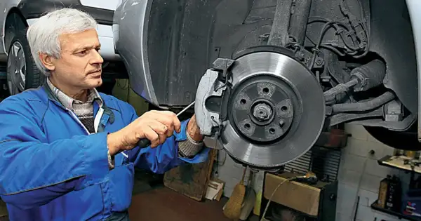 Mechanik w niebieskim kombinezonie naprawia hamulce, wymieniając klocki. W tle widać elementy układu kierowniczego i pompowtryski.