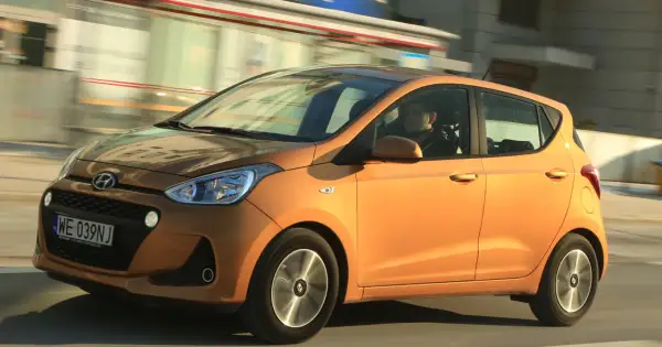 Pomarańczowy Hyundai i10 z kierowcą w środku jedzie ulicą.