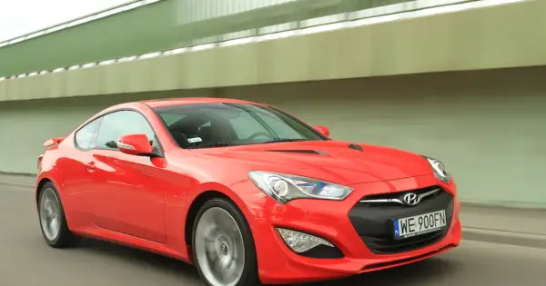 Czerwony Hyundai Genesis Coupe 3.8 V6 w ruchu, z widocznym kierowcą i tablicą rejestracyjną WE 900FN.