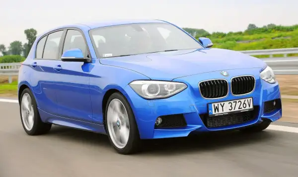 Niebieskie BMW 116i pędzi po drodze, ukazując swoje sportowe linie i dynamiczny charakter.