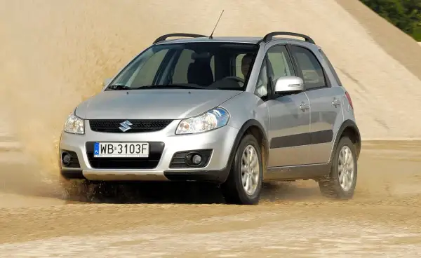 Srebrny Suzuki SX4 1.6 benzyna pokonuje piaszczystą wydmę, wzbijając tumany kurzu.