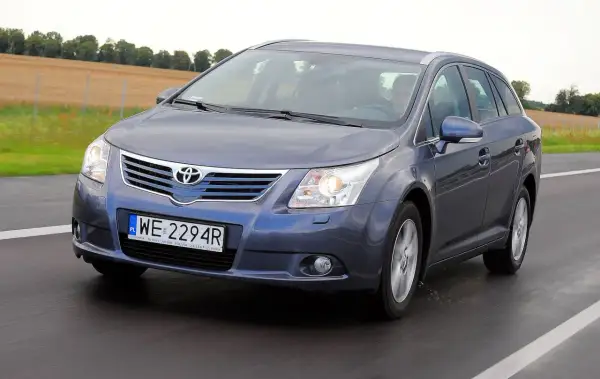 Szary Toyota Avensis T27 1.8 benzyna w kombi jedzie po drodze, za nim pola.