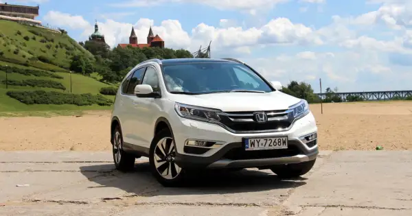 Biała Honda CR-V 2.0 benzyna na tle piaszczystego brzegu i zielonego wzgórza z budynkami.