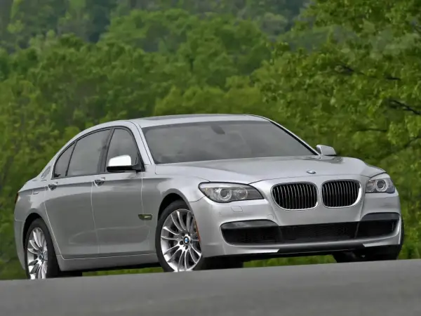 Srebrne BMW 7 F01 na tle zielonych drzew. Elegancka limuzyna prezentuje się okazale na drodze.