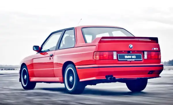 Czerwone BMW E30 Coupe M3 w ruchu, z widocznym spojlerem i podwójnym wydechem.