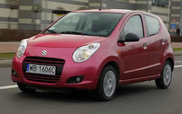 Czerwony Suzuki Alto z polskimi tablicami rejestracyjnymi WB 1606C jedzie po drodze.