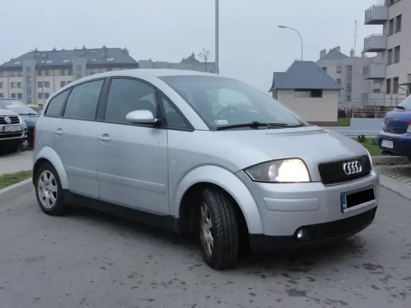 Srebrne Audi A2 zaparkowane przed blokami mieszkalnymi.