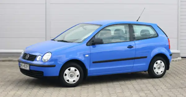Niebieski Volkswagen Polo 1.2 benzyna, widok z boku. Auto stoi na kostce brukowej przed szarym budynkiem.