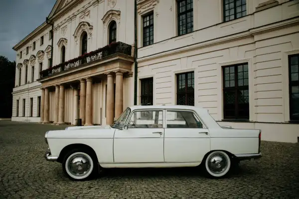 Biały Peugeot 404 na brukowanym dziedzińcu przed pałacem.