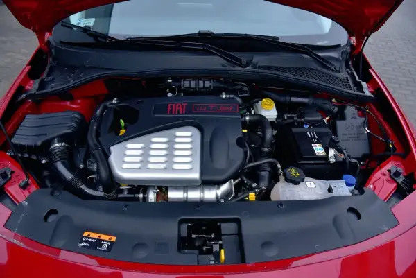 Silnik fiat bravo 1.4 t-jet w komorze pod czerwonym lakierem. Widoczny akumulator, przewody i osłony.