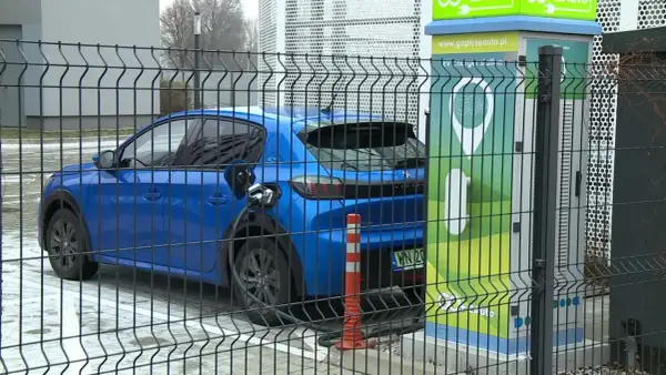 Niebieski samochód elektryczny podłączony do ładowarki. Zastanawiasz się, ile waży samochód elektryczny? Ten model jest lekki i ekologiczny.