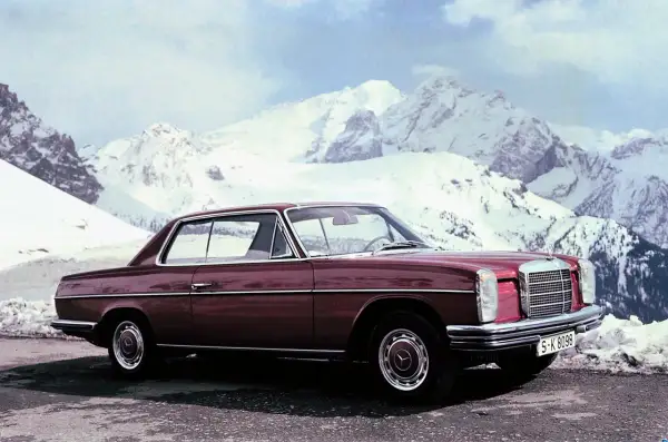 Ciemnoczerwony Mercedes W114 coupe na tle ośnieżonych gór. Klasyka motoryzacji w zimowej scenerii.