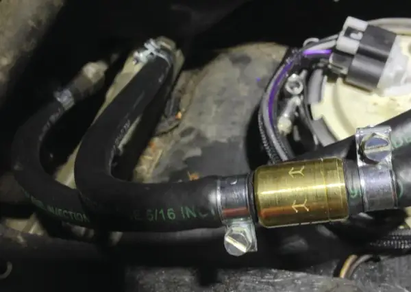 Złoty zawór zwrotny paliwa zamontowany na czarnym wężu paliwowym z oznaczeniem "FUEL INJECTION".