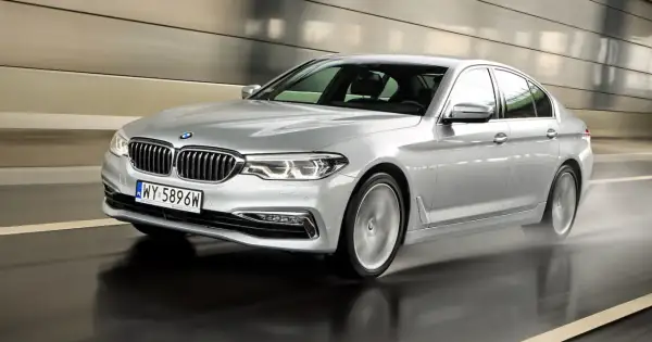 Srebrne BMW 520d xDrive pędzi po mokrej drodze w tunelu, rozpryskując wodę.