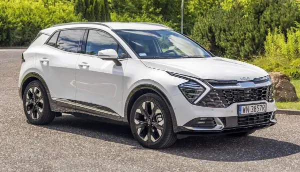 Biały Kia Sportage 1.6 benzyna zaparkowany na tle zieleni. Nowoczesny design i eleganckie felgi.