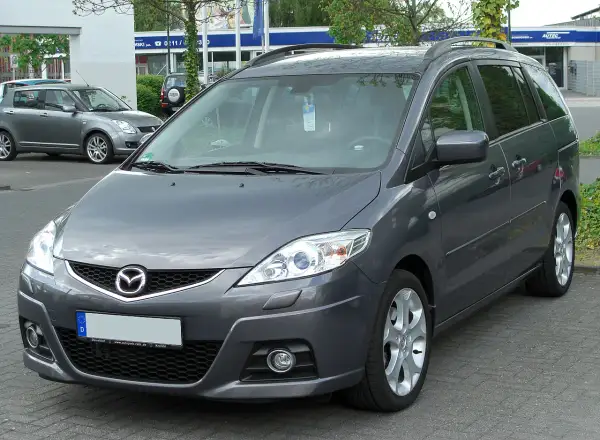 Szary Mazda Premacy stoi na parkingu. W tle widać inne samochody i budynki.