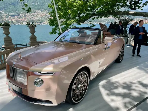 Elegancki Rolls-Royce Boat Tail w kolorze szampańskim, prezentowany nad jeziorem Como, przyciąga wzrok swoim unikalnym designem.