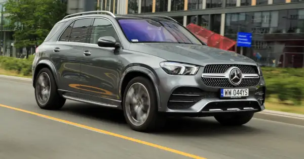 Szary Mercedes GLE 300d jedzie po drodze, w tle nowoczesne budynki.