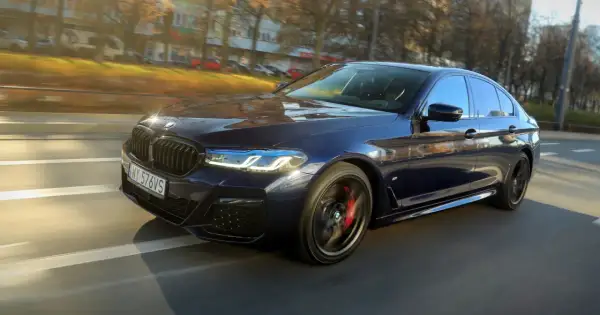 Ciemnoniebieskie BMW 540d w ruchu ulicznym, z widocznymi światłami LED i czerwonymi zaciskami hamulcowymi.