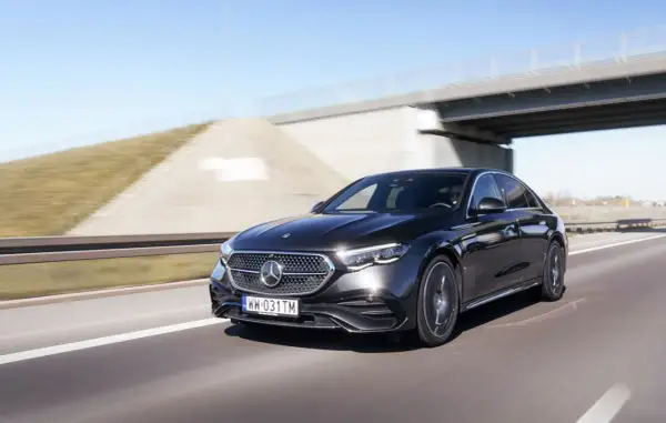Czarny Mercedes E220d pędzi autostradą pod mostem.