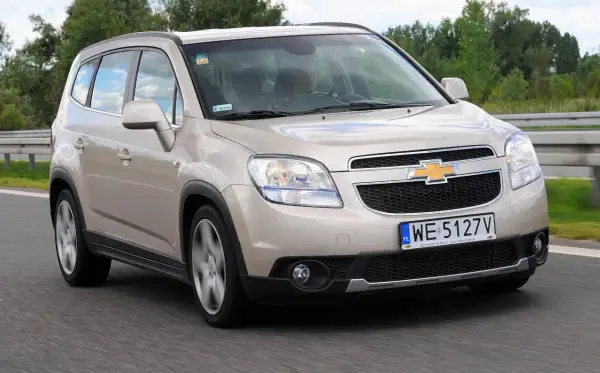 Złoty Chevrolet Orlando na drodze. Kierowca w środku, widok z przodu. Wiele osób szuka chevrolet orlando opinie przed zakupem.