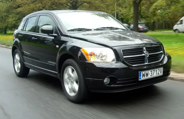 Czarny Dodge Caliber 1.8, jaki to silnik? Auto jedzie po mokrej drodze, w tle drzewa.