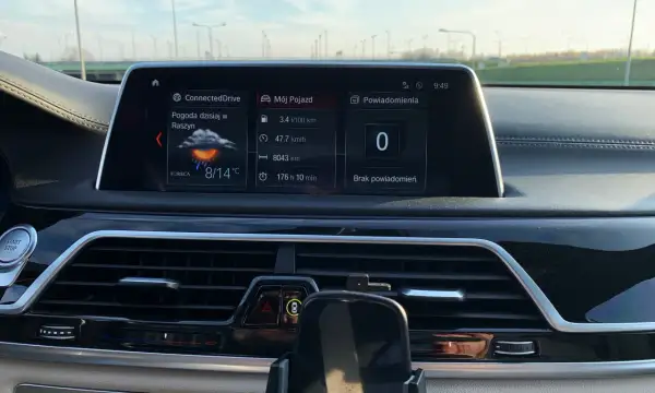 Wnętrze BMW hybryda: ekran z pogodą w Raszynie (8/14°C), spalaniem 3.4l/100km i przebiegiem 8043km.
