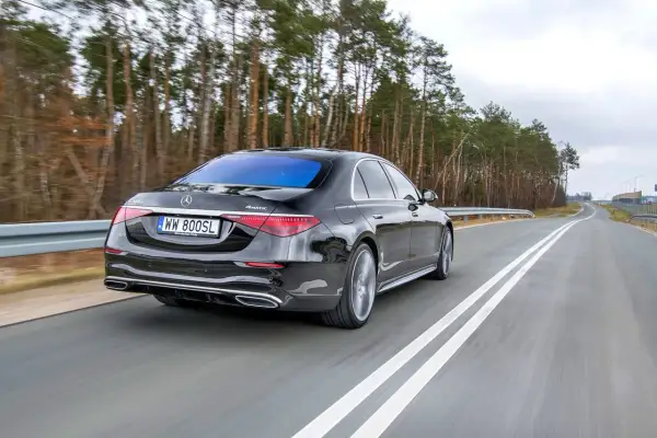 Czarny Mercedes S400d 4Matic z tablicą WW 800SL jedzie po drodze wśród drzew.