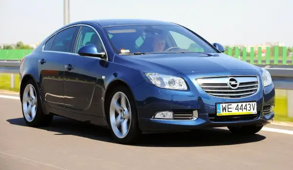 Niebieski Opel Insignia 1.6 Turbo pędzi po drodze. Kierowca wpatrzony w horyzont.