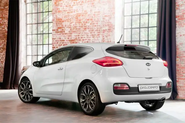 Biały Kia Ceed 2012, widok z tyłu, stoi w studiu z ceglaną ścianą i dużymi oknami.