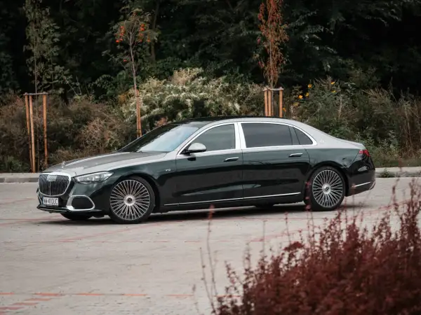 Elegancki Maybach S680 w ciemnozielonym kolorze z dwukolorowym nadwoziem, zaparkowany na tle jesiennej zieleni.